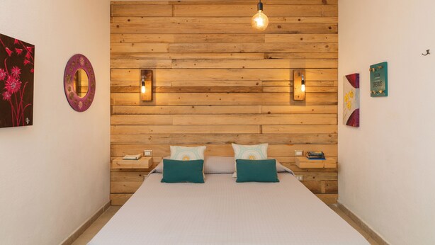 Een slaapkamer met een houten hoofdbord, twee nachtkastjes, een bed met teal kussens en wandlampen.