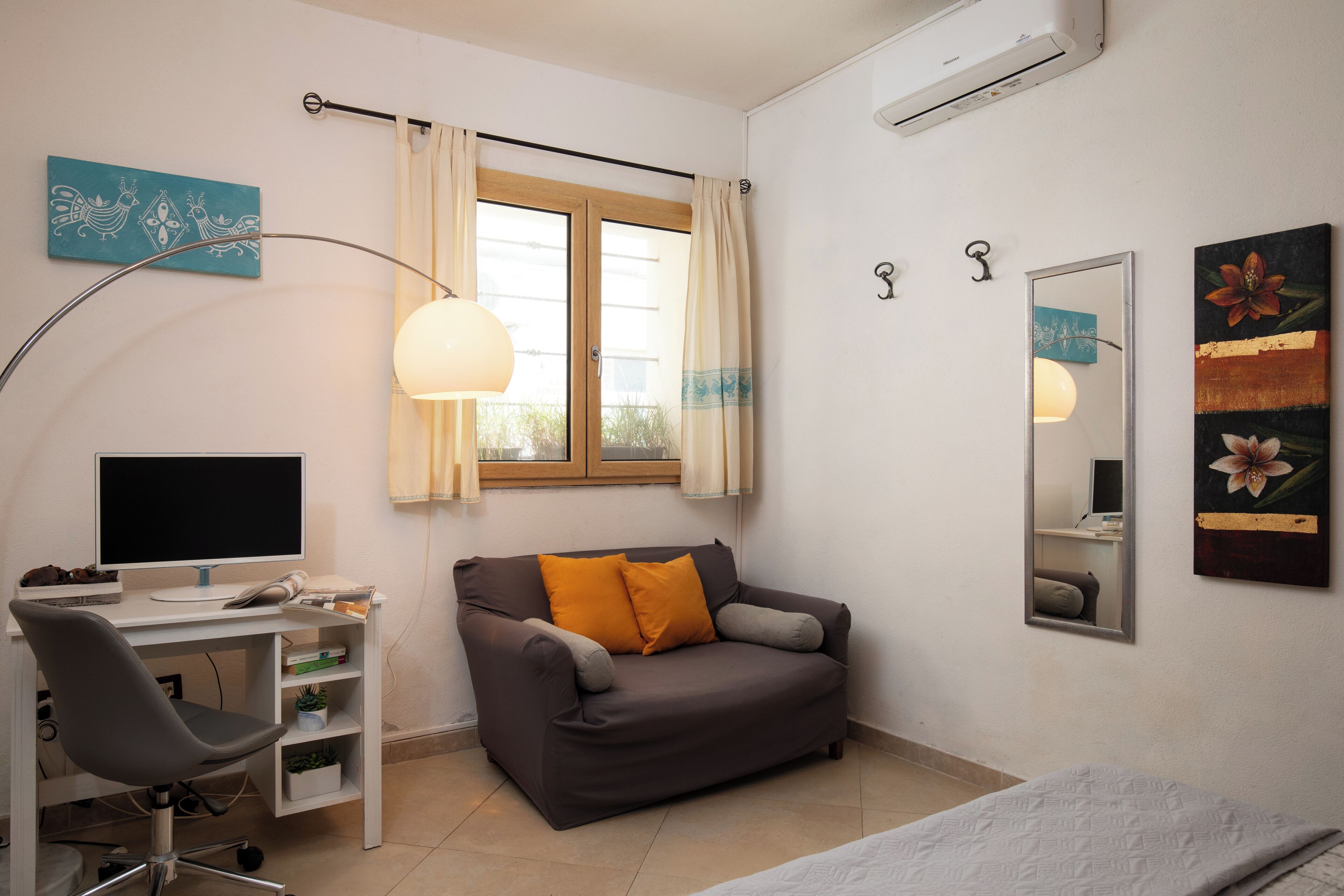 Habitación compacta con escritorio, sofá, cama, espejo y ventana con cortinas.