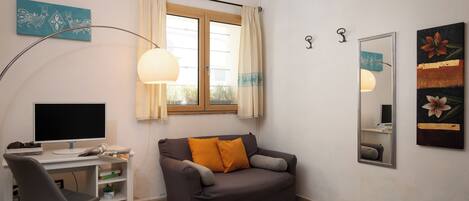 Habitación compacta con escritorio, sofá, cama, espejo y ventana con cortinas.