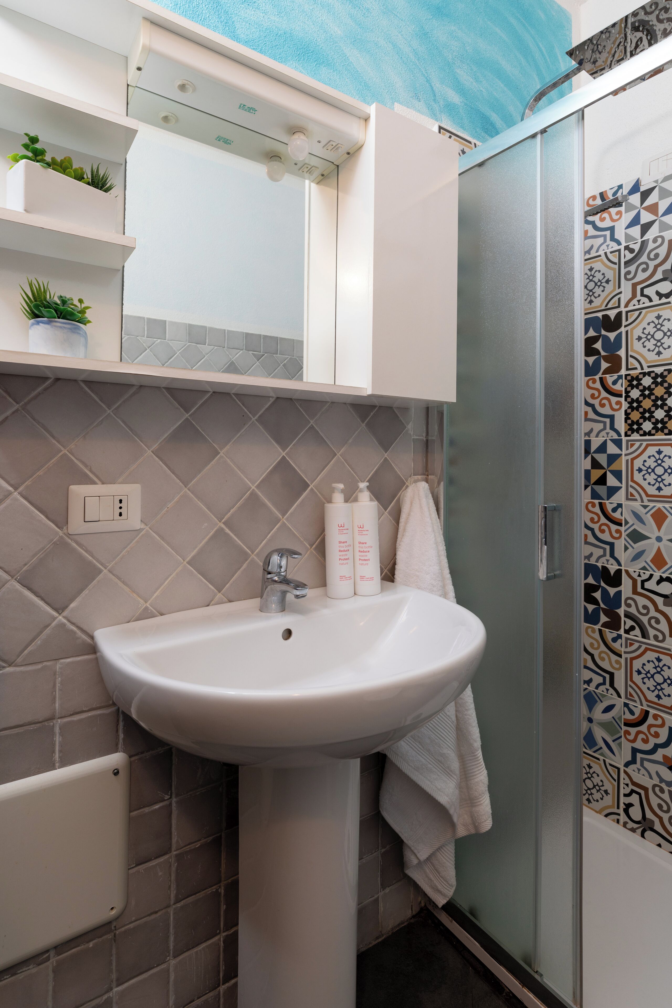 A bathroom with a white sink, a mirror above it, and a shower with patterned tiles.