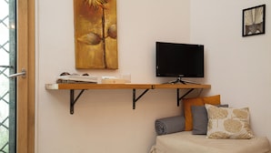 Een kamer met een televisie op een plank, een schilderij aan de muur en een bed met kussens.