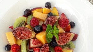 A white square plate with a variety of fresh fruits including kiwi, blueberries, raspberries, and melon.