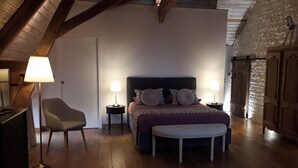 A bedroom with a bed, bedside tables, a chair, an ottoman, and a wardrobe.