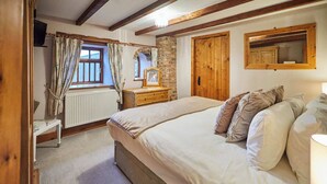 Ein Schlafzimmer mit einem großen Bett, Holzbalken, einer Ziegelwand, einem Fenster mit Vorhängen, einem Schminktisch und einem Spiegel.