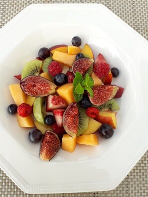 Une assiette carrée blanche garnie d’une variété de fruits frais, notamment des kiwis, des myrtilles, des framboises et du melon.