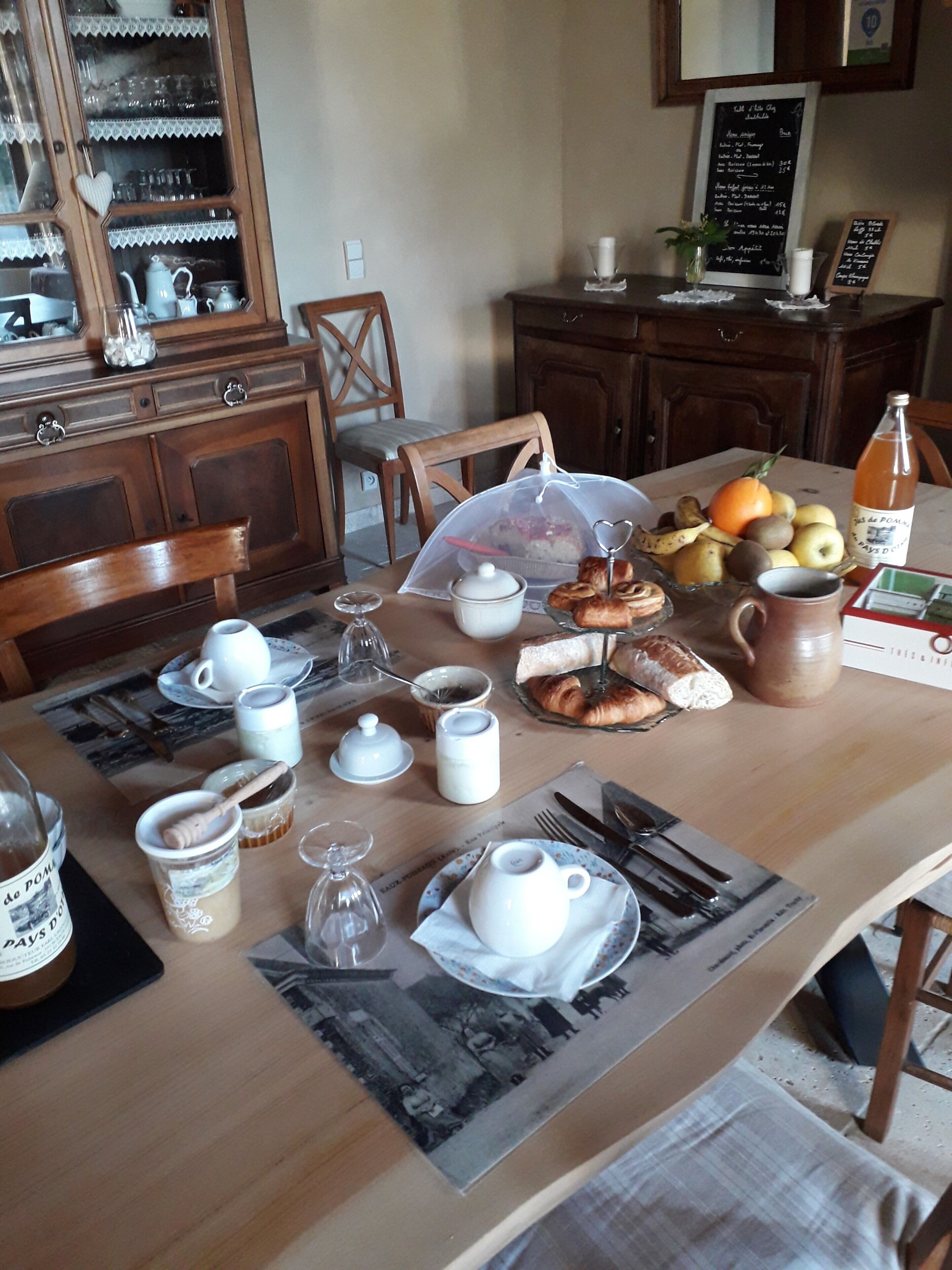 Ein Esstisch ist reichhaltig mit Frühstücksleckereien gedeckt, darunter Gebäck, Früchte und eine Saftflasche.