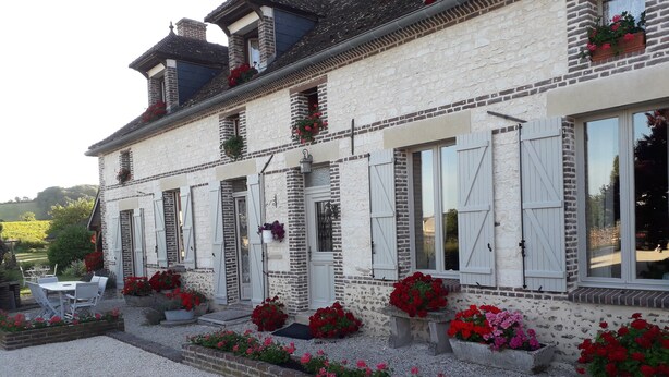 Un edificio con fachada de piedra, varias ventanas con contraventanas y jardineras con flores.