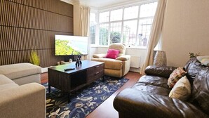 A living room with a sofa, armchair, and a television on a stand. - Spacious Home Near Wembley with Parking & Garden (Harrow)