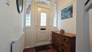 A hallway with a white door, a wooden dresser, and a painting on the wall. - Spacious Home Near Wembley with Parking & Garden (Harrow)
