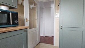 A kitchen with a microwave, a trash bin, and a door leading to another room. - Spacious Home Near Wembley with Parking & Garden (Harrow)
