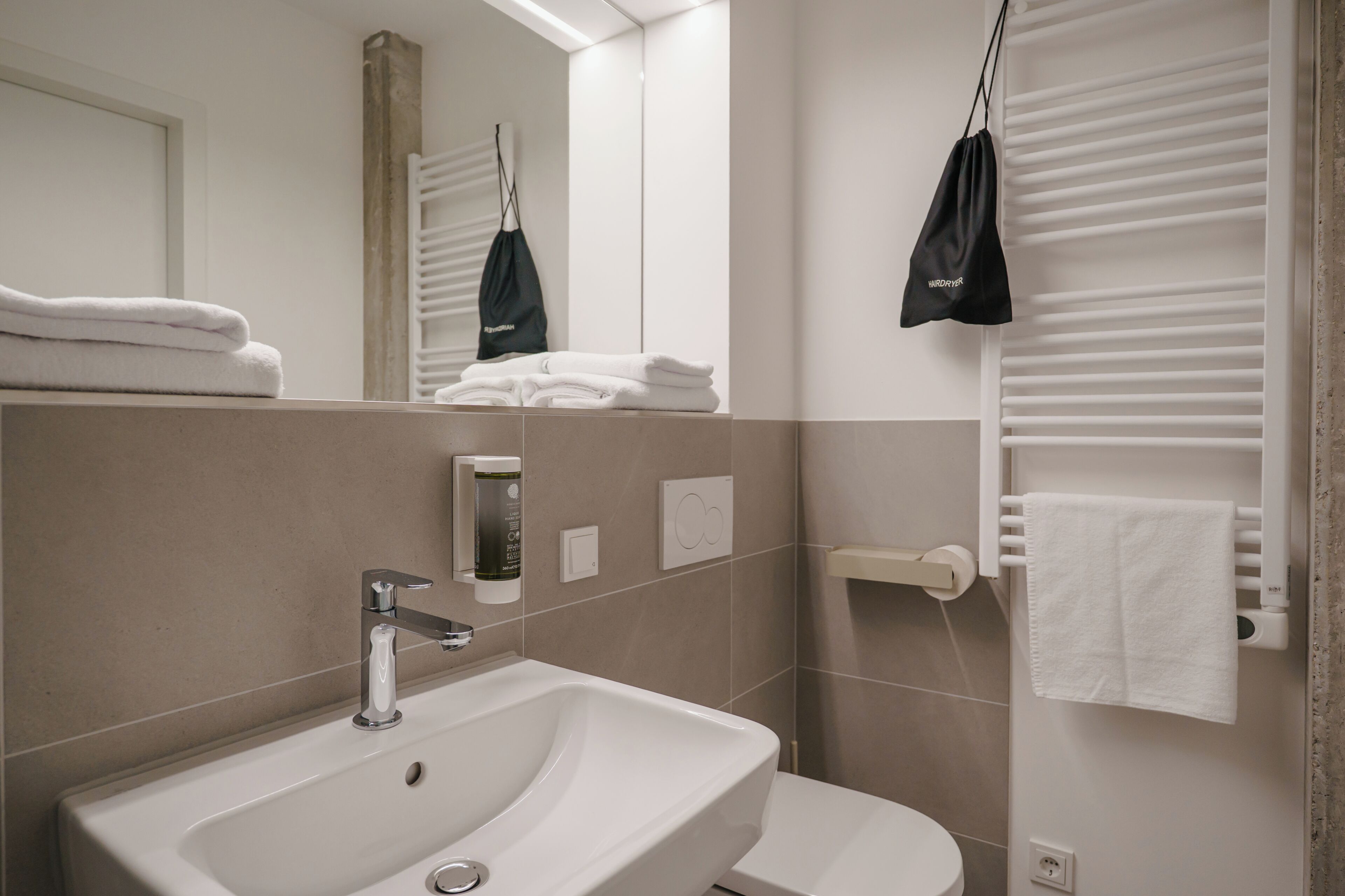 Une salle de bain moderne équipée d’un lavabo, d’un miroir, d’un porte-serviettes et d’un sèche-serviettes.