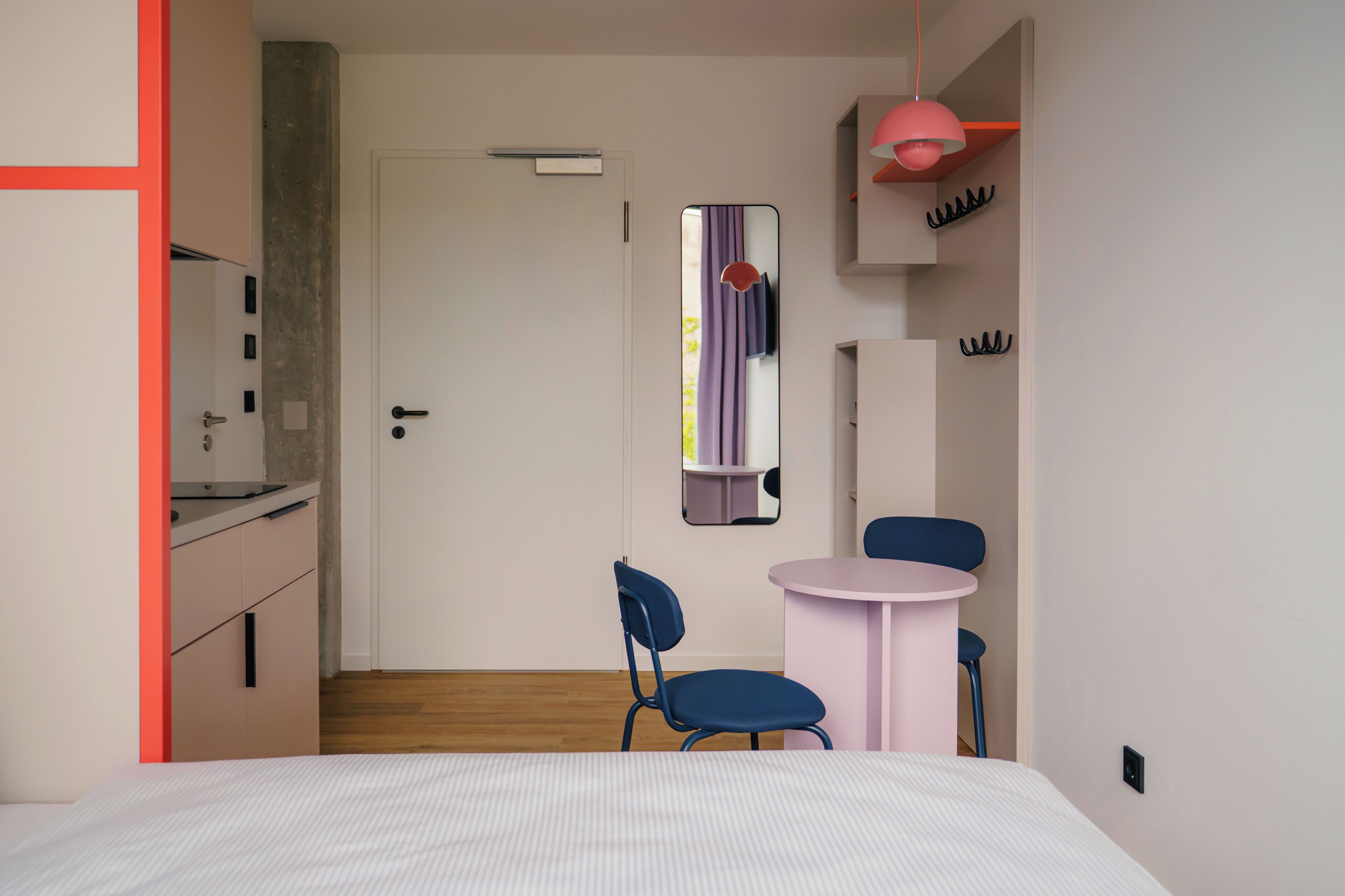 Un dormitorio moderno con una cama, dos sillas, una mesita, un espejo y una puerta que da al baño.