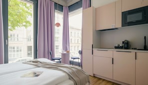 A modern hotel room with a bed, a small kitchenette, and a view of the city. - Homaris K48 Studios (Berlin)