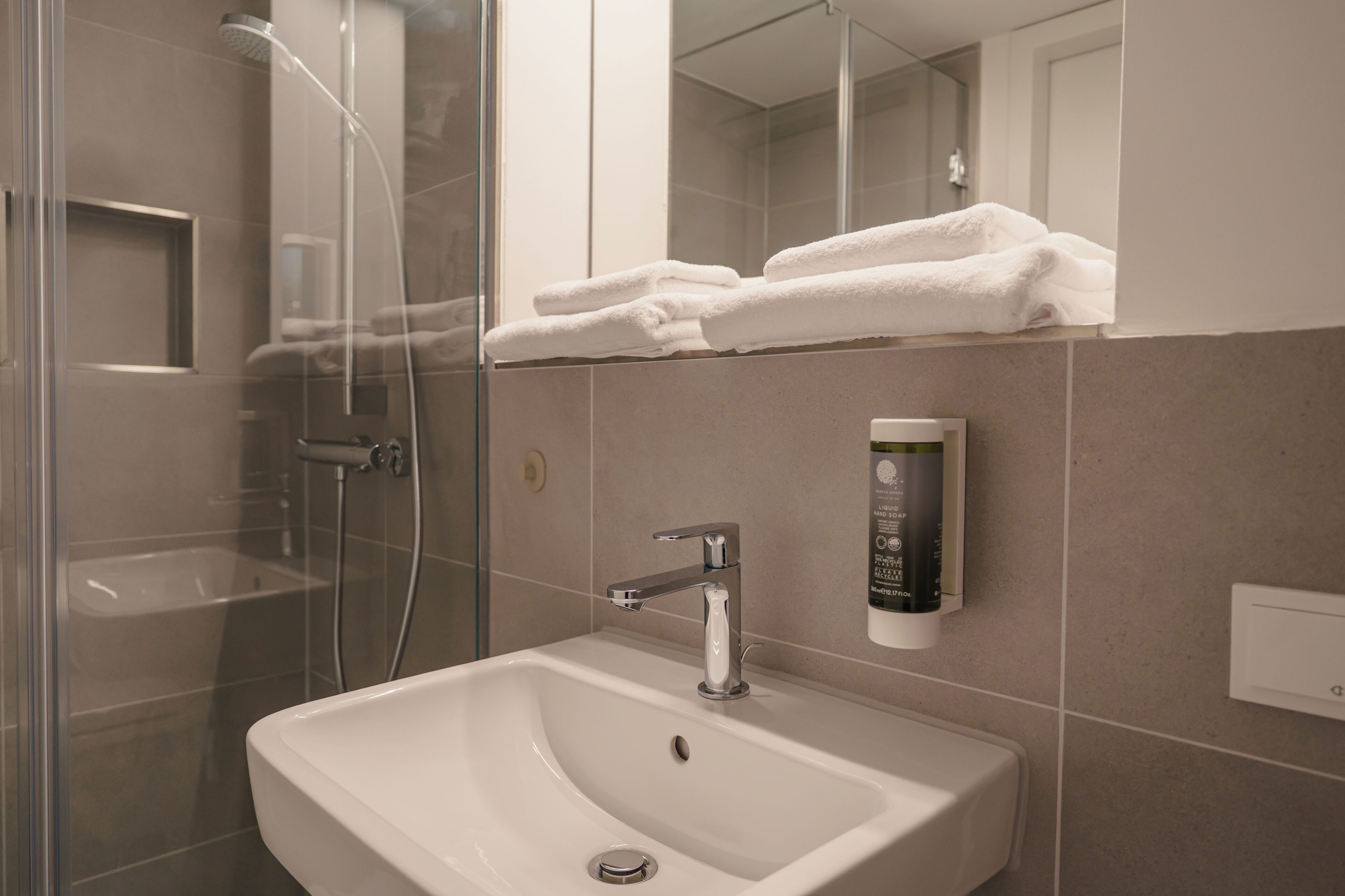 A modern bathroom with a glass shower enclosure, a white sink, and a towel rack with folded towels.