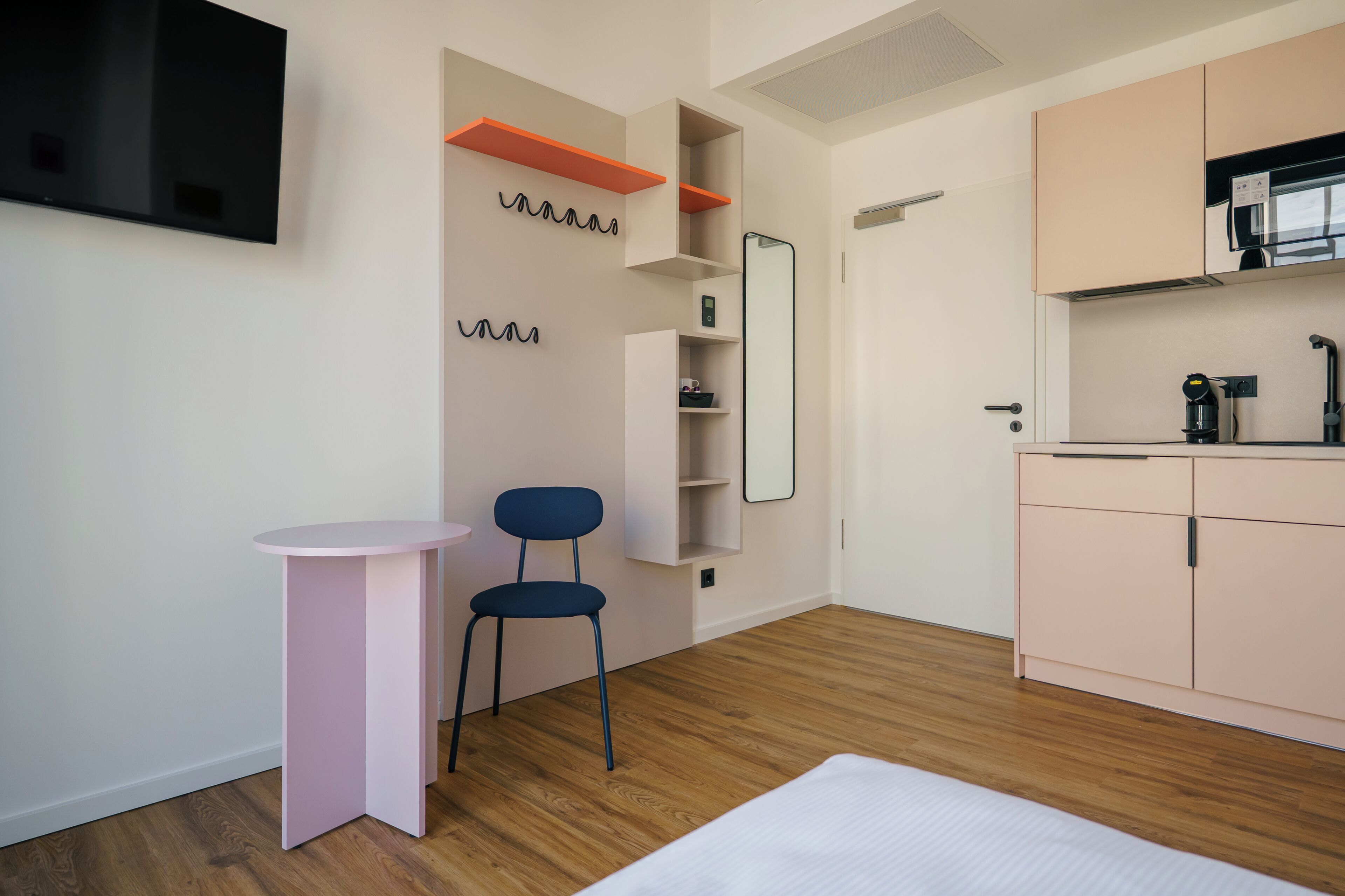 A modern, compact room with a kitchenette, a small seating area, and a bed.