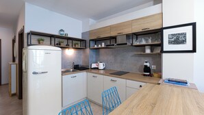 A compact kitchen with a white refrigerator, wooden cabinets, a countertop with a coffee maker, and a framed picture on the wall. - Welcoming 1-bedroom apartment  in charming Sozopol (Sozopol)