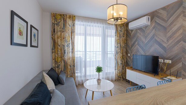A modern living room with a sofa, a round table, a TV, and a plant. - Welcoming 1-bedroom apartment  in charming Sozopol (Sozopol)