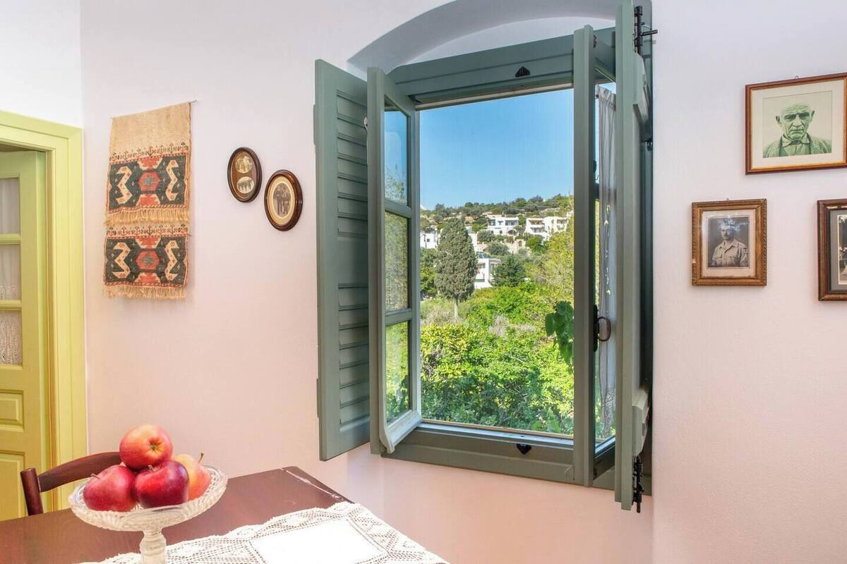 A room with a window overlooking a residential area, a table with apples, and several framed pictures on the wall.