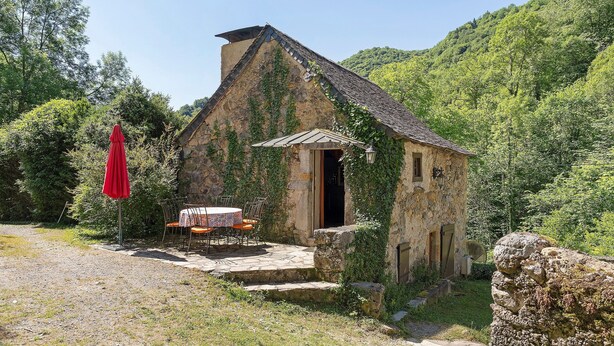 Un bâtiment en pierre doté d’un petit porche et d’un parasol rouge.