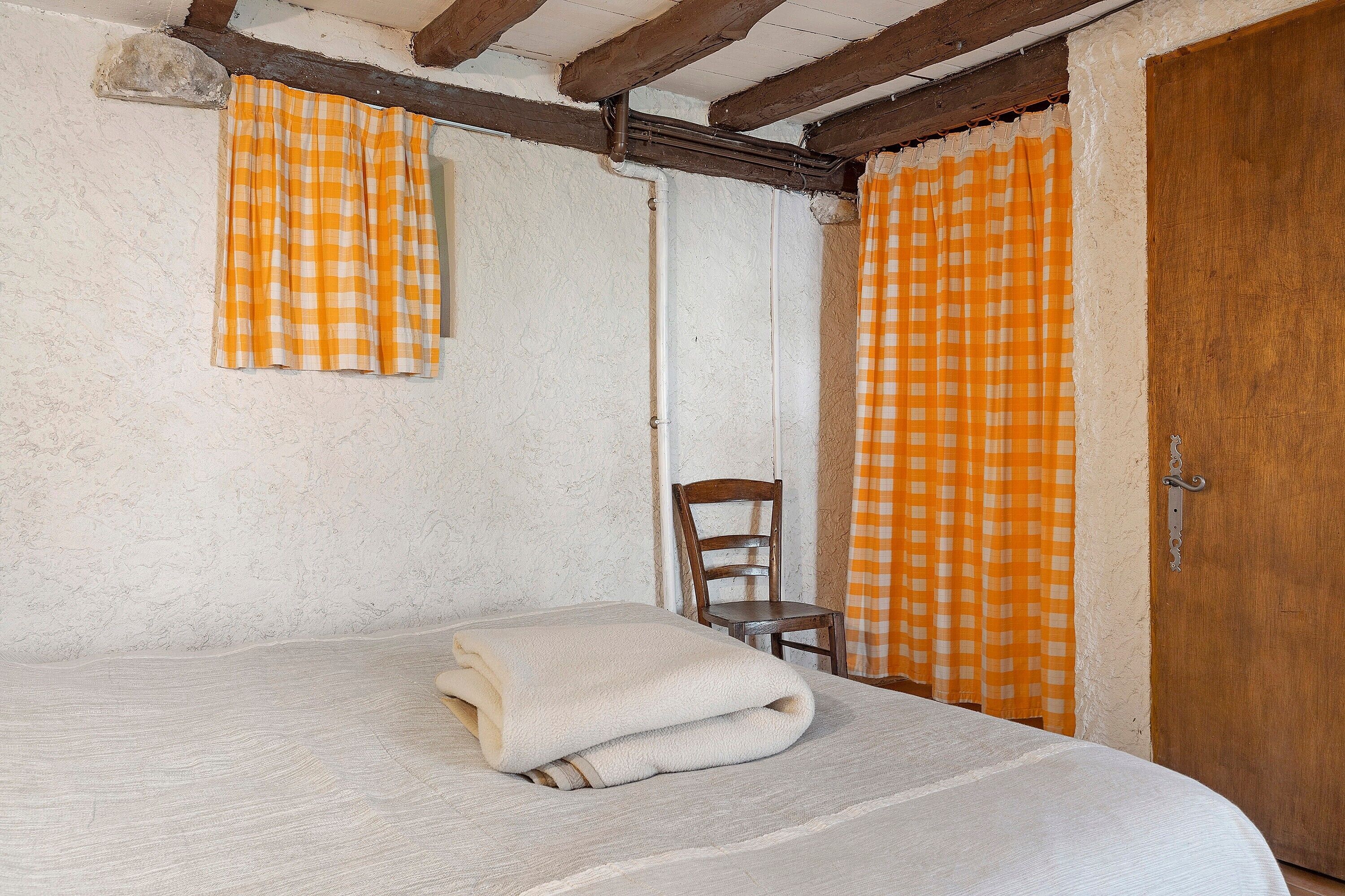 Ein Zimmer mit einem Bett, einem Stuhl und einer Holztür.