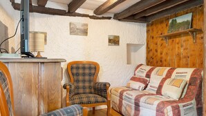 Une pièce chaleureuse avec un plafond en bois, un fauteuil à carreaux, un canapé agrémenté de coussins à motifs et une petite table avec une lampe.