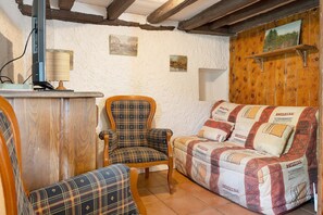 A cozy room with a wooden ceiling, a plaid armchair, a sofa with patterned cushions, and a small table with a lamp. - Small House on 5 Hectares with Pool, Sauna, Gym, Horses, Donkey (Osse-en-Aspe)