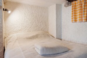 A room with a textured white wall, a bed with a white blanket, a stone accent, and a checkered curtain. - Small House on 5 Hectares with Pool, Sauna, Gym, Horses, Donkey (Osse-en-Aspe)