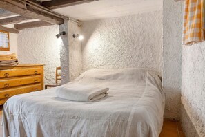 A bedroom with a bed, wooden dresser, and a textured wall. - Small House on 5 Hectares with Pool, Sauna, Gym, Horses, Donkey (Osse-en-Aspe)
