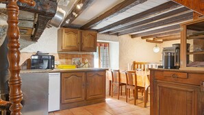 Une cuisine avec des meubles de rangement en bois, une table à manger, des chaises, un réfrigérateur et une machine à café.