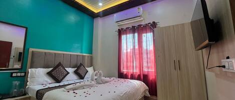 A modern hotel room with a bed, a ceiling fan, an air conditioning unit, a TV mounted on the wall, and a window with red curtains.
