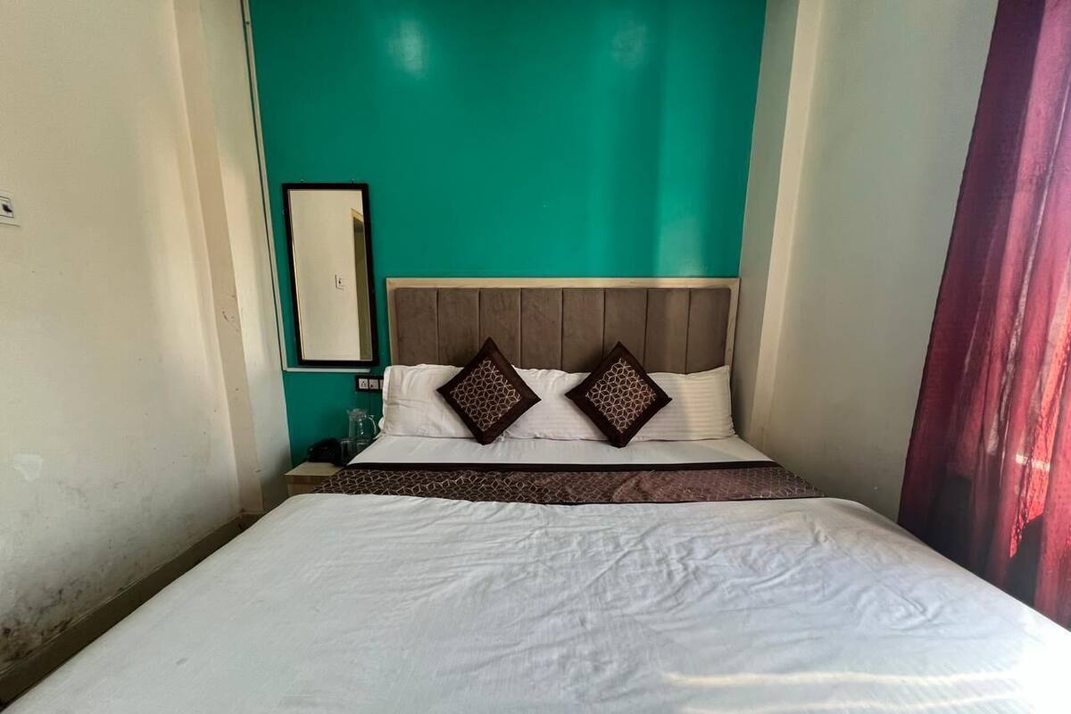A neatly made bed with white linens and two decorative pillows, a wooden headboard, and a teal accent wall.