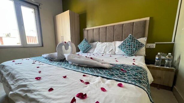A neatly made bed with rose petals, a wooden headboard, and a green patterned bedspread. - Shri Hari Kripa Residency (Varanasi)