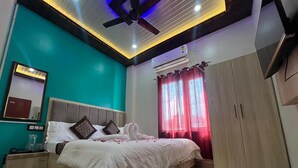A modern bedroom with a bed, a ceiling fan, an air conditioning unit, a wardrobe, and a television. - Shri Hari Kripa Residency (Varanasi)