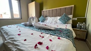 A neatly made bed with rose petals, a wooden headboard, and a bedside table with water bottles. - Shri Hari Kripa Residency (Varanasi)
