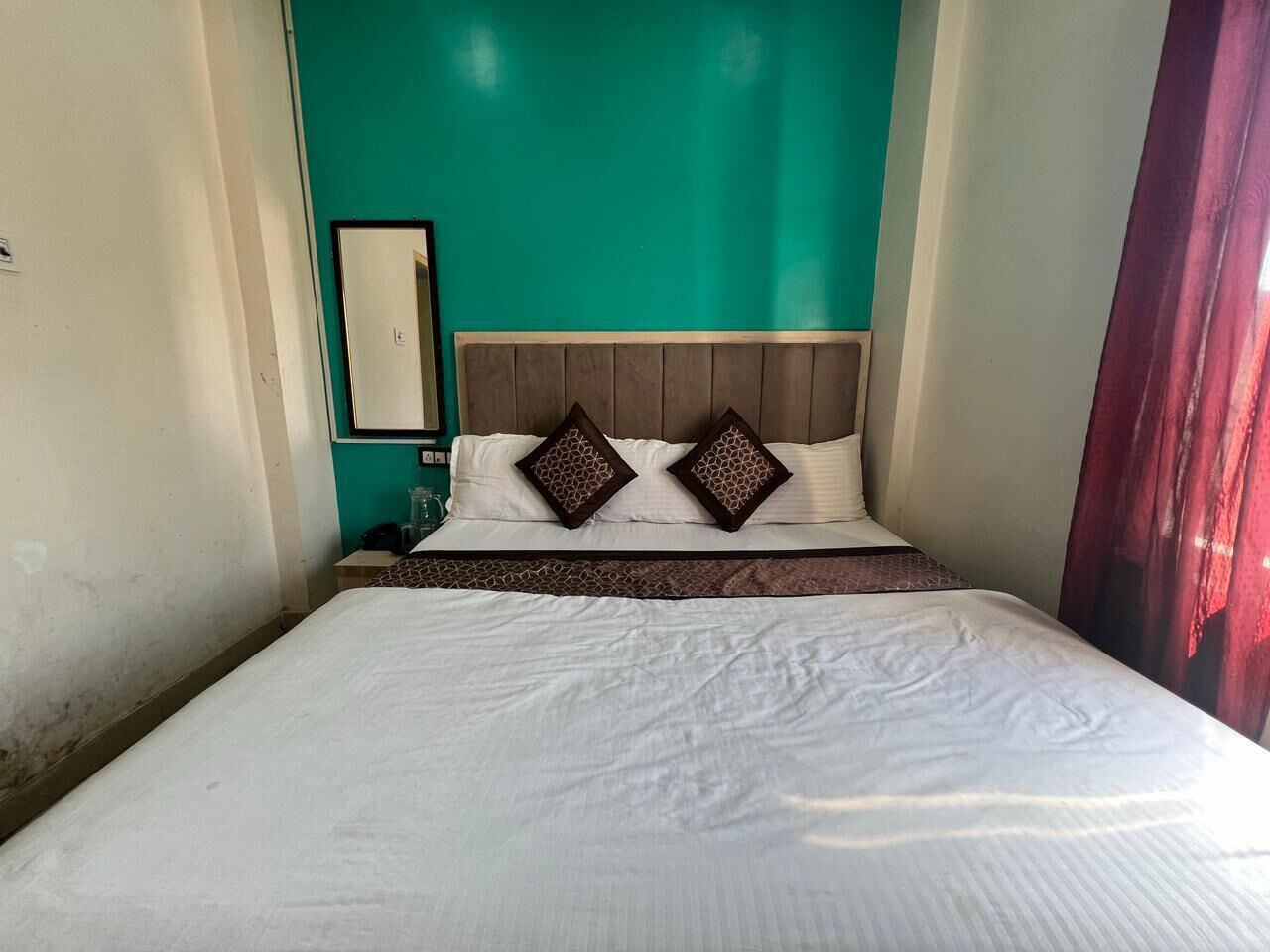 A bed with white bedding, two decorative pillows, a wooden headboard, and a teal accent wall.