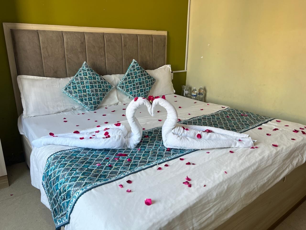 A neatly made bed with a patterned bedspread, two pillows, and two swans made of towels.