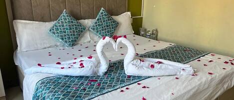 A neatly made bed with a patterned bedspread, two pillows, and two swans made of towels.