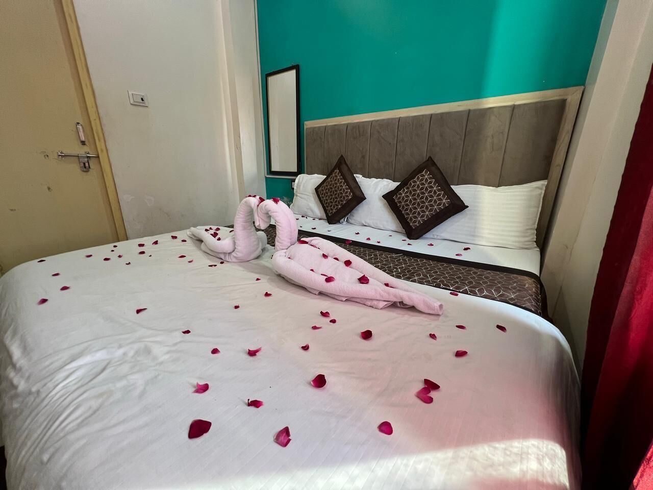A hotel room with a bed adorned with rose petals and a towel arranged in a heart shape.