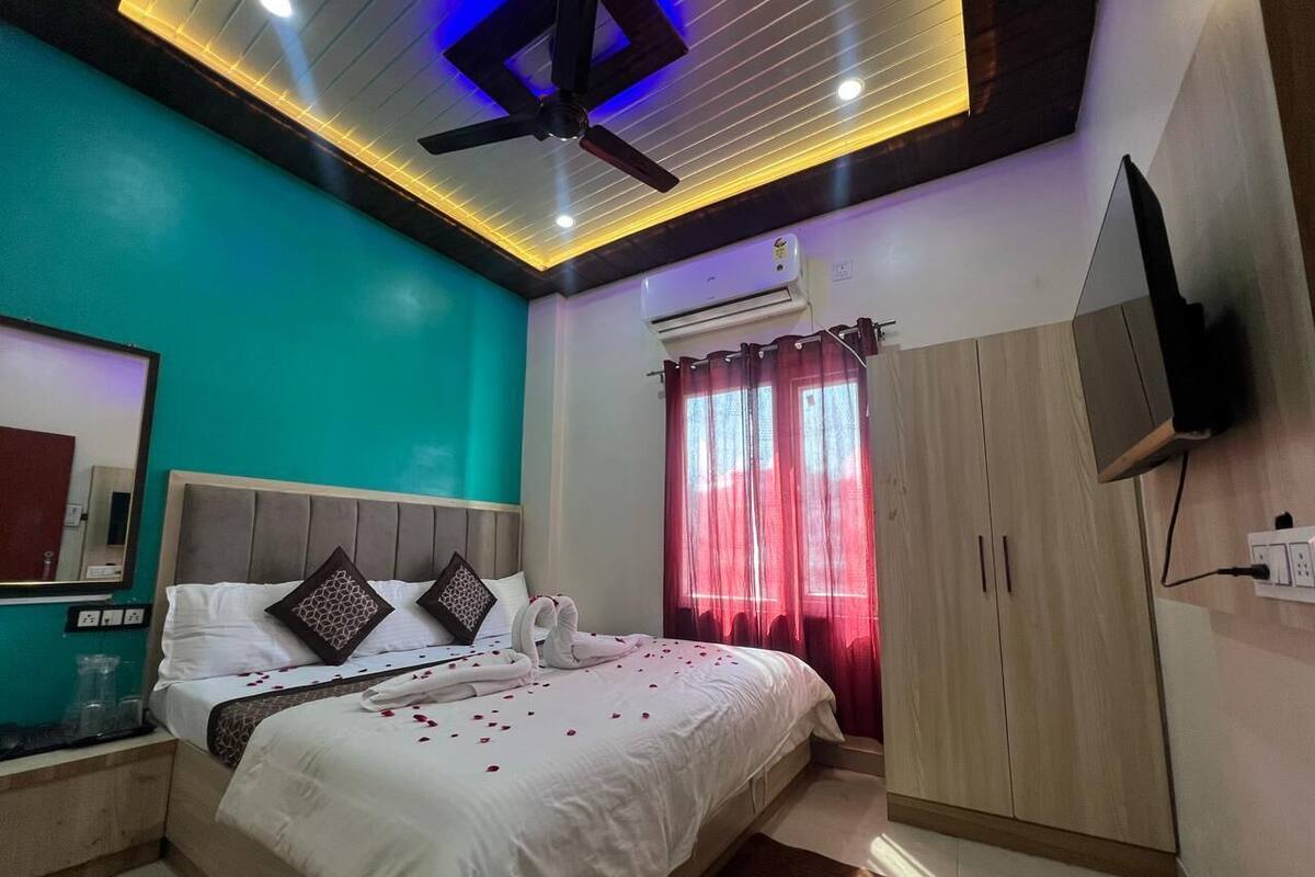 A modern bedroom with a bed, a ceiling fan, an air conditioner, a wardrobe, and a TV mounted on the wall.