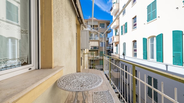 Ein Balkon mit kleinem Tisch und Bank, der auf eine enge Straße mit Häusern blickt.