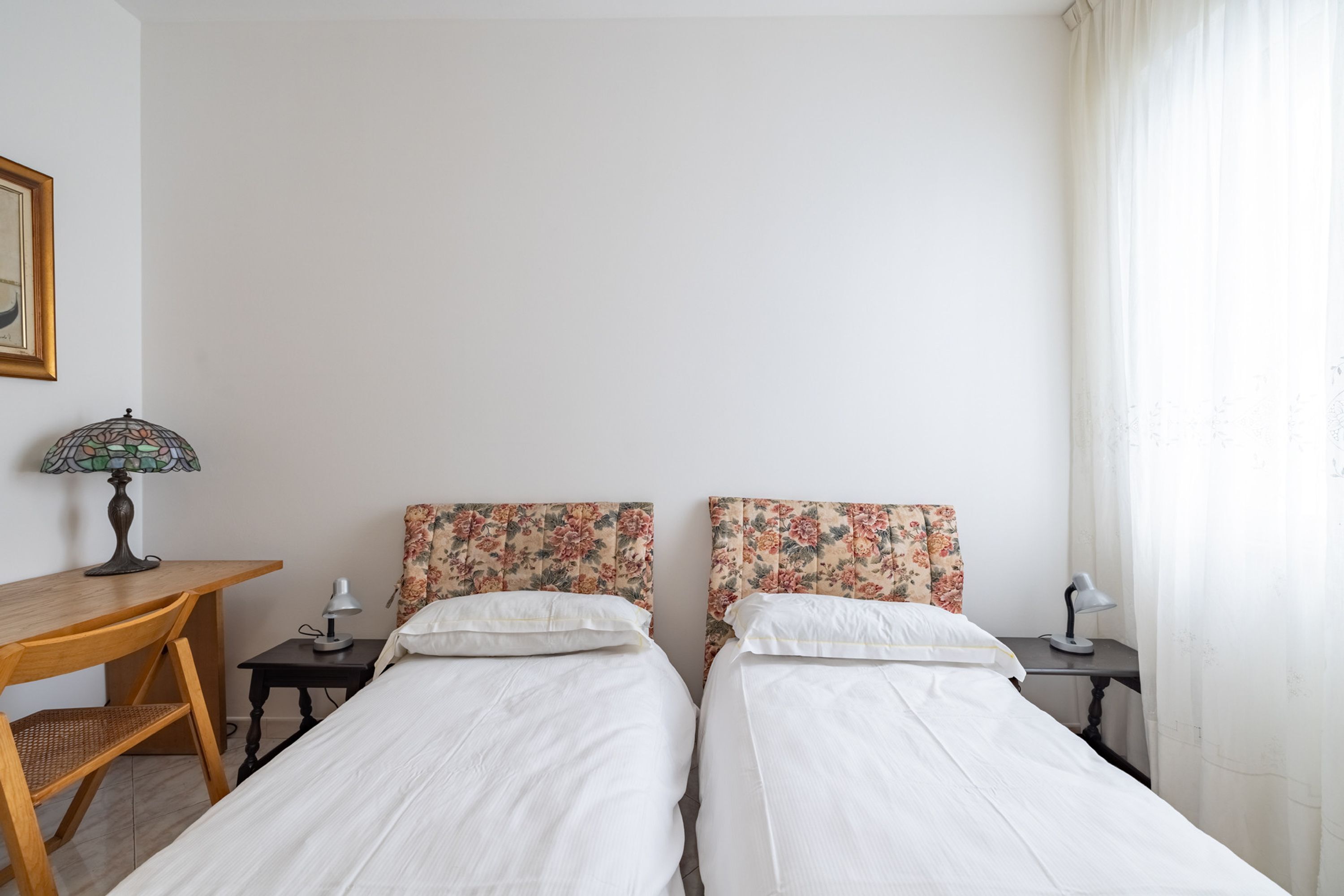 A room with two single beds, a wooden desk, a small table, and a lamp.