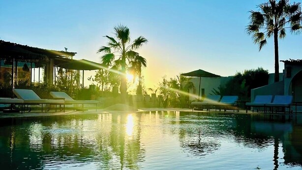 A tranquil pool area with lounge chairs and palm trees, surrounded by buildings with large windows and a clear sky. - La villa DUCASSE (Ounagha)