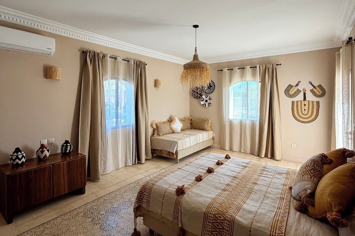 A bedroom with a bed, a bedside table, a dresser, a hanging light fixture, and a window with curtains.