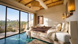 A bedroom with a large window, a bed, a hanging light fixture, and a view of the outdoors. - La villa DUCASSE (Ounagha)