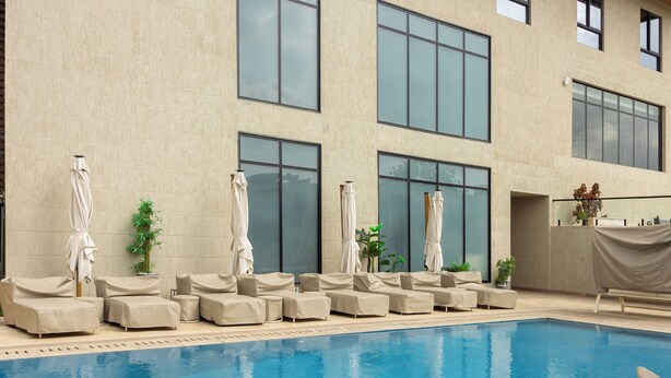 Area piscina con diverse poltrone prendisole e ombrelloni, una piscina piastrellata e un edificio con ampie finestre.