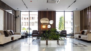 Una hall moderna con una grande composizione floreale, due divani, un tavolo da pranzo e un'ampia finestra con vista su edifici e alberi.