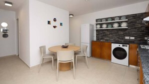Uma cozinha compacta com máquina de lavar embutida, área de jantar com mesa redonda e cadeiras, e prateleira fixada na parede com pratos decorativos.