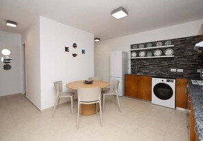 Une cuisine compacte dotée d’un lave-linge intégré, d’un coin repas avec une table ronde et des chaises, et d’une étagère murale ornée d’assiettes décoratives.