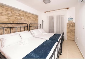 A double room with two beds, a stone accent wall, a sign reading "Relax", and a window with sheer curtains.