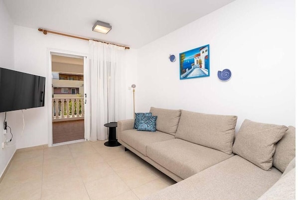 A living room with a beige sofa, a flat-screen TV, a painting, and a small table.